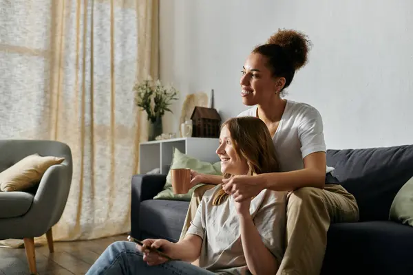 A lesbian couple relaxes on a couch in a home, enjoying each others company and a casual afternoon. — Stock Photo