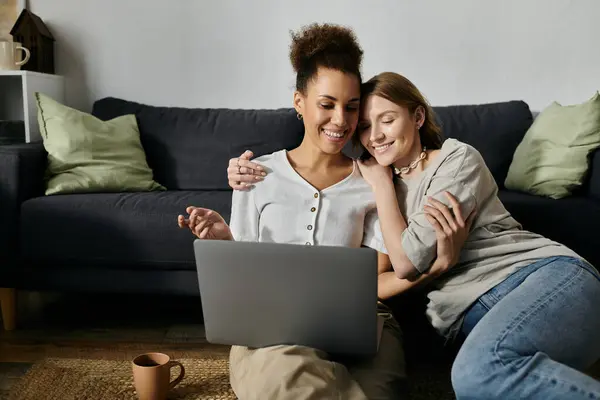 Una coppia lesbica coccola sul pavimento nella loro casa mentre guarda un computer portatile. — Foto stock