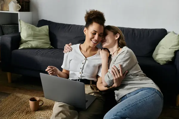 Una coppia lesbica varia si coccola insieme sul pavimento, sorridendo e ridendo mentre utilizza un computer portatile. — Foto stock