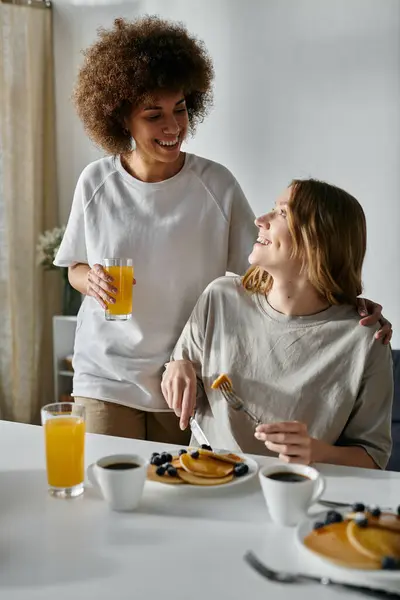 Deux femmes partagent un moment d'amour autour d'un petit déjeuner de crêpes et de jus d'orange. — Photo de stock