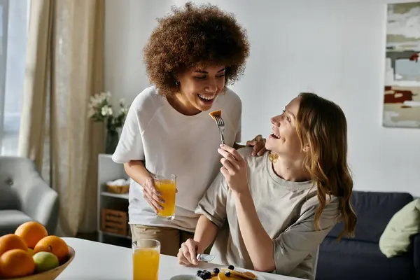 Una coppia lesbica si gode una colazione insieme a casa, ridendo e condividendo un pasto. — Foto stock