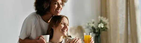 A lesbian couple enjoying each others company at home, with one holding a mug and the other holding a glass of juice. — Stock Photo