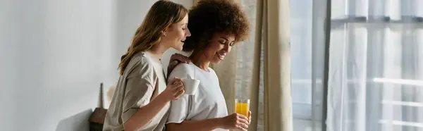 A diverse lesbian couple shares a moment of intimacy at home, enjoying coffee and orange juice. — Stock Photo