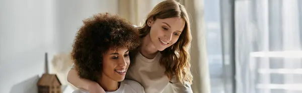 Two women, one with long blonde hair and the other with short curly black hair, cuddle together at home. — Stock Photo