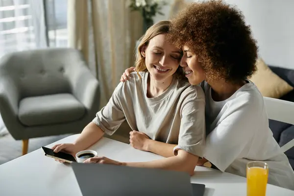 Two women, a lesbian couple, cuddle while using a laptop and enjoying a beverage. — Stock Photo
