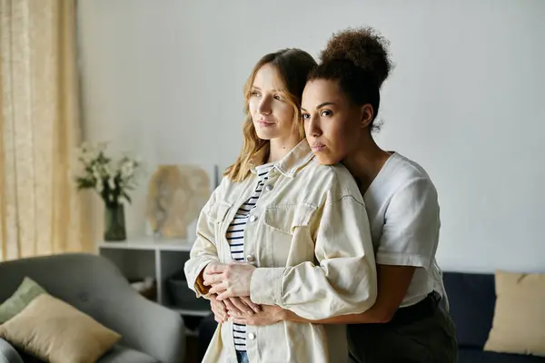 Two women, embracing in a loving gesture, stand by a window with sunlight streaming through. — Stock Photo
