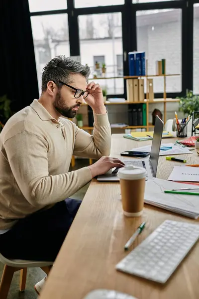 Un bell'uomo d'affari con la barba lavora su un portatile alla sua scrivania moderna. — Foto stock