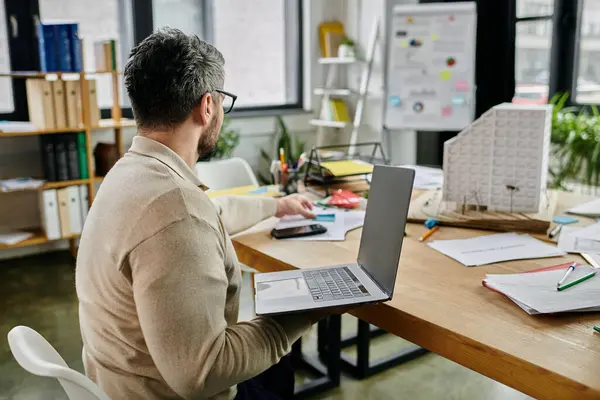 Un homme d'affaires barbu travaille sur un ordinateur portable à un bureau encombré dans un bureau moderne. — Photo de stock