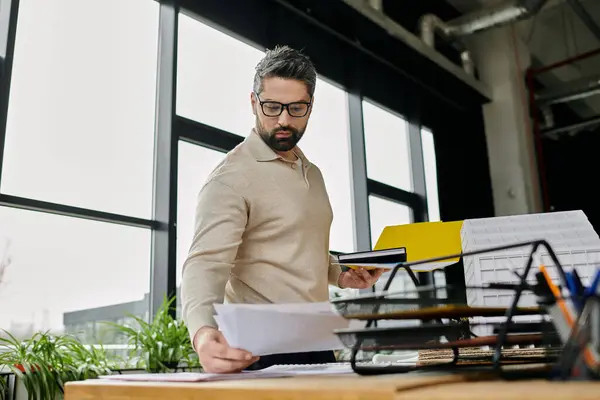 A handsome businessman with a beard examines documents in a modern office setting. — Stock Photo