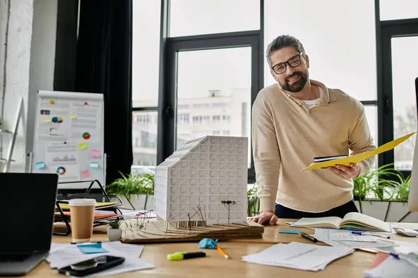 Um homem de negócios bonito com uma barba analisa plantas e um edifício modelo em um escritório moderno. — Fotografia de Stock