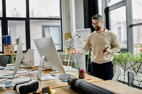 Um empresário barbudo de óculos está em um escritório moderno, apontando para uma tela de computador enquanto discute um projeto. — Fotografia de Stock