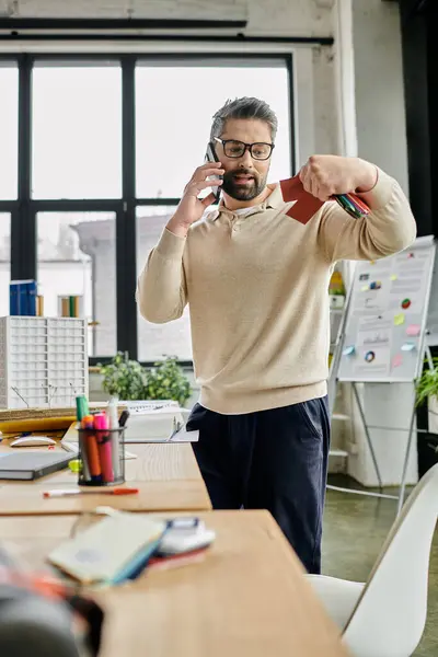 Красивый бизнесмен с бородой говорит по телефону, стоя в современном офисе. — стоковое фото