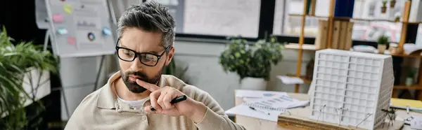 A handsome businessman with a beard and glasses sits in a modern office, pen in hand, thoughtfully considering his next move. — Stock Photo