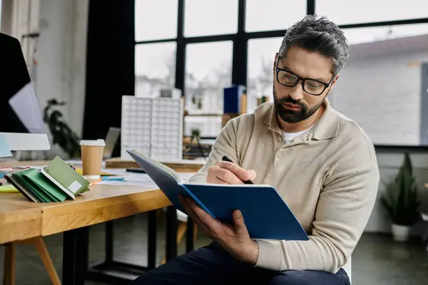 A businessman with a beard works in a modern office, writing in a blue notebook. — Stock Photo