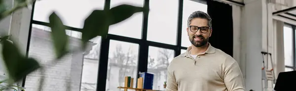 A handsome businessman with a beard, wearing glasses, smiles confidently while standing in a modern office setting. — Stock Photo