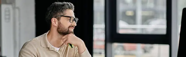 Um belo homem de negócios com barba se senta em sua mesa em um escritório moderno, olhando atenciosamente para o lado. — Fotografia de Stock