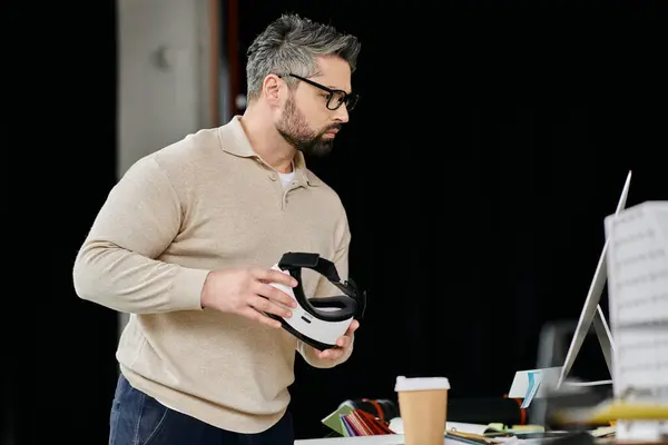 Un bell'uomo d'affari con la barba tiene un auricolare bianco in realtà virtuale in un ambiente ufficio moderno. — Foto stock