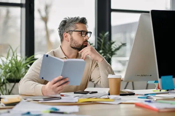 A bearded businessman in a modern office thoughtfully reviews documents, his hand resting on his chin. — Stock Photo