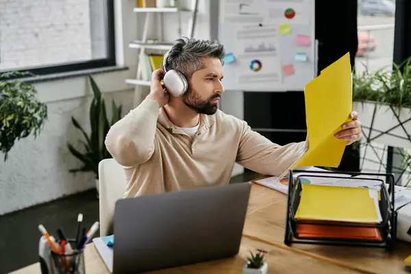 A handsome businessman with a beard works diligently in a modern office, reviewing documents while wearing headphones. — Stock Photo