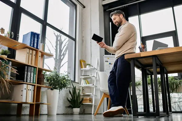 Um belo homem de negócios com barba está em um escritório moderno, revisando um projeto em seu tablet. — Fotografia de Stock