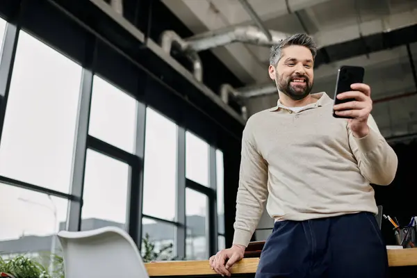 A handsome businessman with a beard smiles as he looks at his phone in a modern office. — Stock Photo