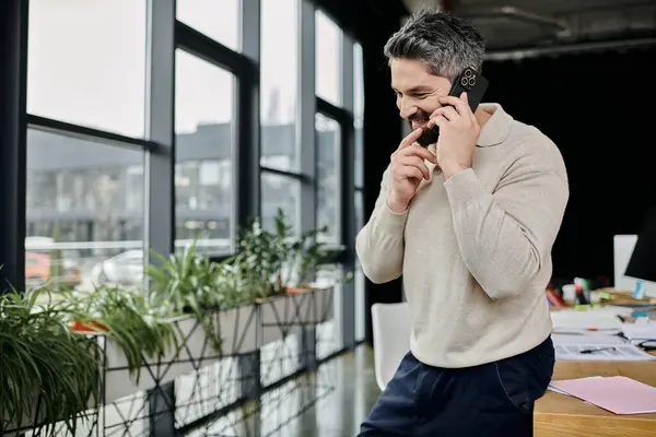 A handsome businessman with a beard smiles while making a phone call in a modern office setting. — Stock Photo