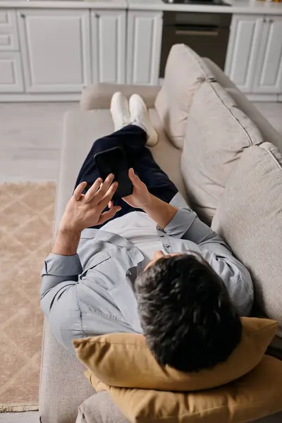 A bearded man is relaxing on a sofa in his home while checking his phone. — Stock Photo