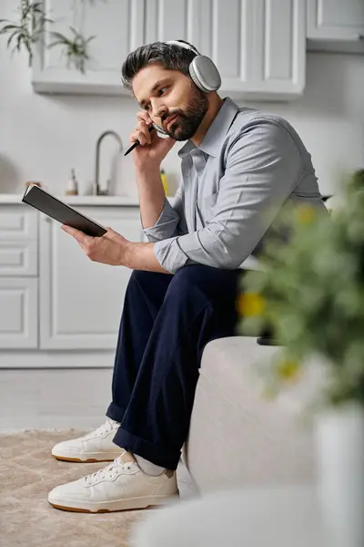 A bearded man in casual attire sitting on a couch with a notebook and headphones. — Stock Photo