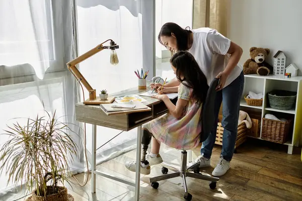 Una madre bruna e sua figlia con una gamba protesica trascorrono del tempo di qualità a casa, riunendosi su una scrivania. — Foto stock