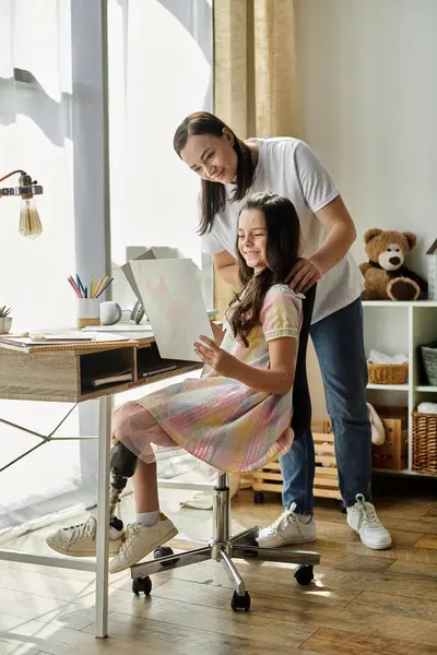 Una madre y su hija están pasando tiempo de calidad juntos en casa, la hija está sentada en una silla, mirando algo en sus manos. - foto de stock