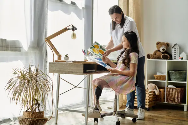 Une mère brune et sa fille avec une jambe prothétique passent du temps ensemble à la maison, dessinant et appréciant l'autre compagnie. — Photo de stock