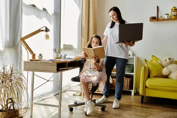 Una madre e sua figlia sono sedute a una scrivania, la figlia che legge un libro e la madre che guarda un portatile. — Foto stock