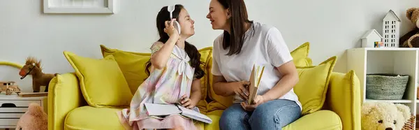 A brunette mother and her daughter with a prosthetic leg are enjoying quality time together on a yellow sofa at home. — Stock Photo