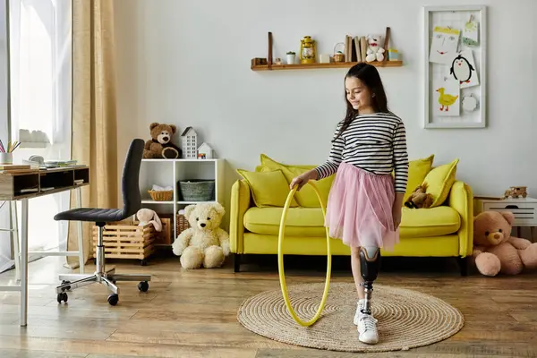 A young girl with a prosthetic leg spins a yellow hula hoop in her home living room, surrounded by toys and a yellow couch. — Stock Photo