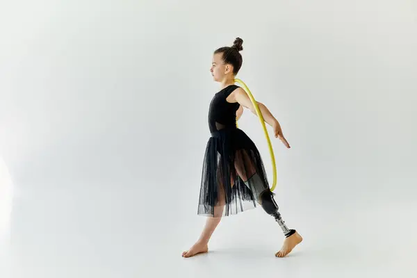 A young girl with a prosthetic leg practices gymnastics while spinning a yellow hoop. — Stock Photo