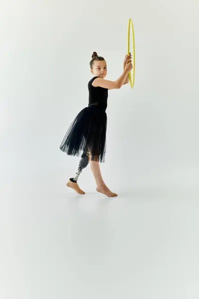 A young girl with a prosthetic leg practices gymnastics with a hula hoop in a studio setting. — Stock Photo