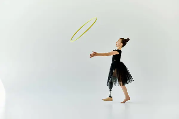 A young girl with a prosthetic leg practices gymnastics with a hula hoop in a white studio. — Stock Photo