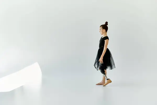 A young girl in a black leotard and tutu stands in a white studio, showcasing her strength and grace while wearing a prosthetic leg. — Stock Photo