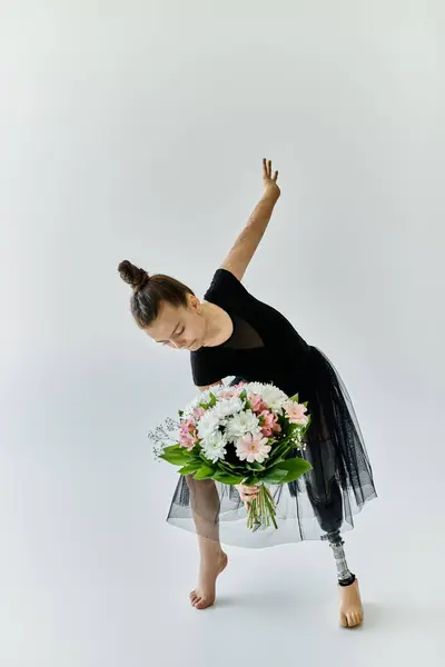 A young girl with a prosthetic leg performs a gymnastic pose while holding a bouquet of flowers. — Stock Photo