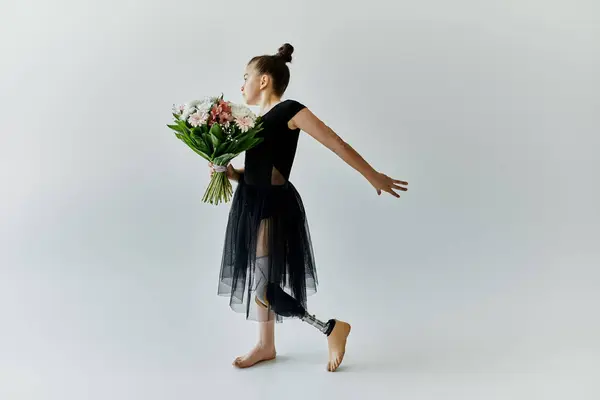 A young girl with a prosthetic leg performs a gymnastic pose while holding a bouquet of flowers. — Stock Photo