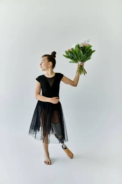 A young girl with a prosthetic leg poses gracefully in a black leotard and tulle skirt, holding a bouquet of flowers. — Stock Photo