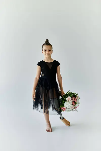 Ein junges Mädchen mit Beinprothese posiert mit Blumen, während sie ein schwarzes Trikot und Tutu trägt. — Stockfoto