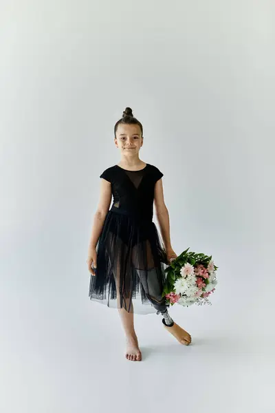 A young girl with a prosthetic leg poses with flowers while wearing a black leotard and tutu. — Stock Photo