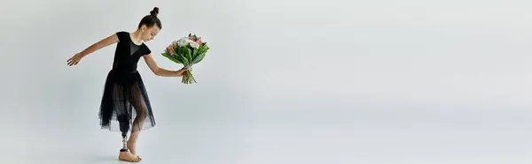 Young girl with a prosthetic leg in a black leotard and tutu poses gracefully holding a bouquet of flowers. — Stock Photo
