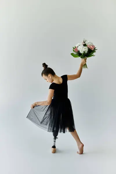A young girl with a prosthetic leg holds a bouquet of flowers while wearing a black leotard and tutu. — Stock Photo