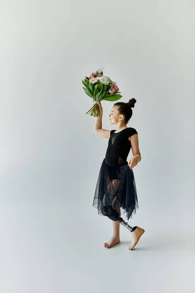 Una joven con una pierna protésica practica gimnasia mientras sostiene un ramo de flores. - foto de stock