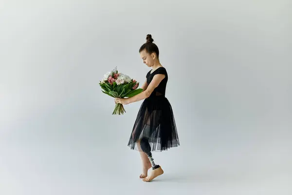 Ein junges Mädchen mit Beinprothese hält einen Blumenstrauß in der Hand, während es ein schwarzes Turntrikot und Tutu trägt. — Stockfoto