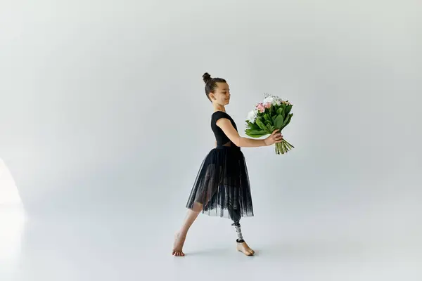 Ein junges Mädchen mit Beinprothese hält anmutig einen Blumenstrauß in einem schwarzen Ballettkleid in einem Studio-Setting. — Stockfoto