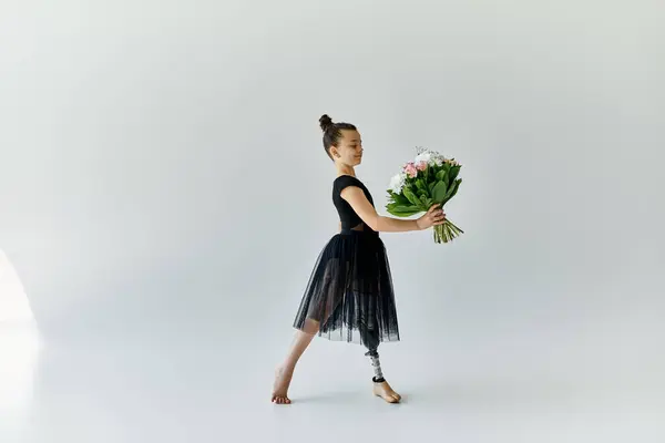 A young girl with a prosthetic leg gracefully holds a bouquet of flowers while wearing a black ballet dress in a studio setting. — Stock Photo