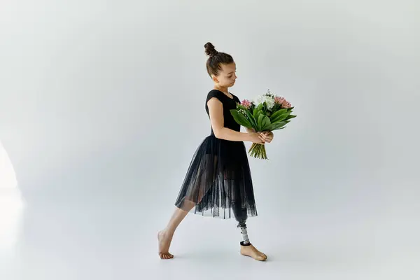 Una giovane ragazza con una gamba protesica posa in uno studio di ginnastica, tenendo un mazzo di fiori. — Foto stock
